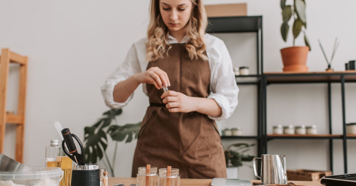 woman in apron making candles on a wooden counter with various ingredients and tools