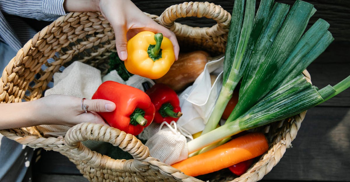 woven basket with fresh vegetables including bell peppers and leeks held by hands outdoors