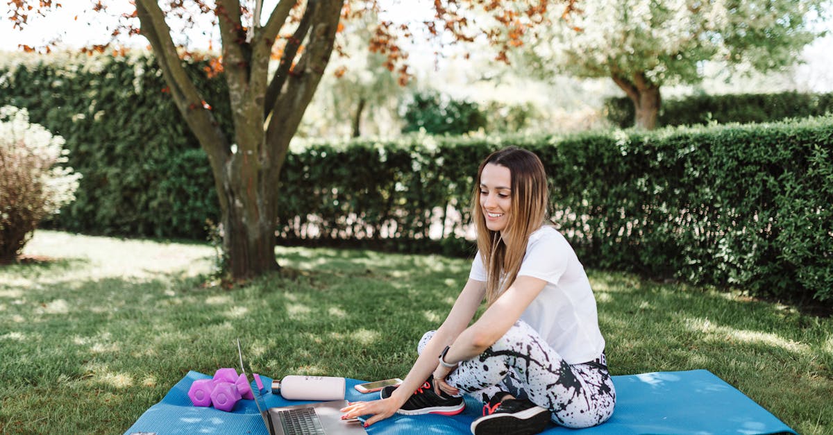 young woman in activewear using a laptop on a yoga mat outdoors enjoying a sunny day