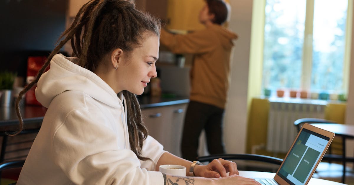 young woman with dreadlocks works on a laptop in a casual kitchen environment